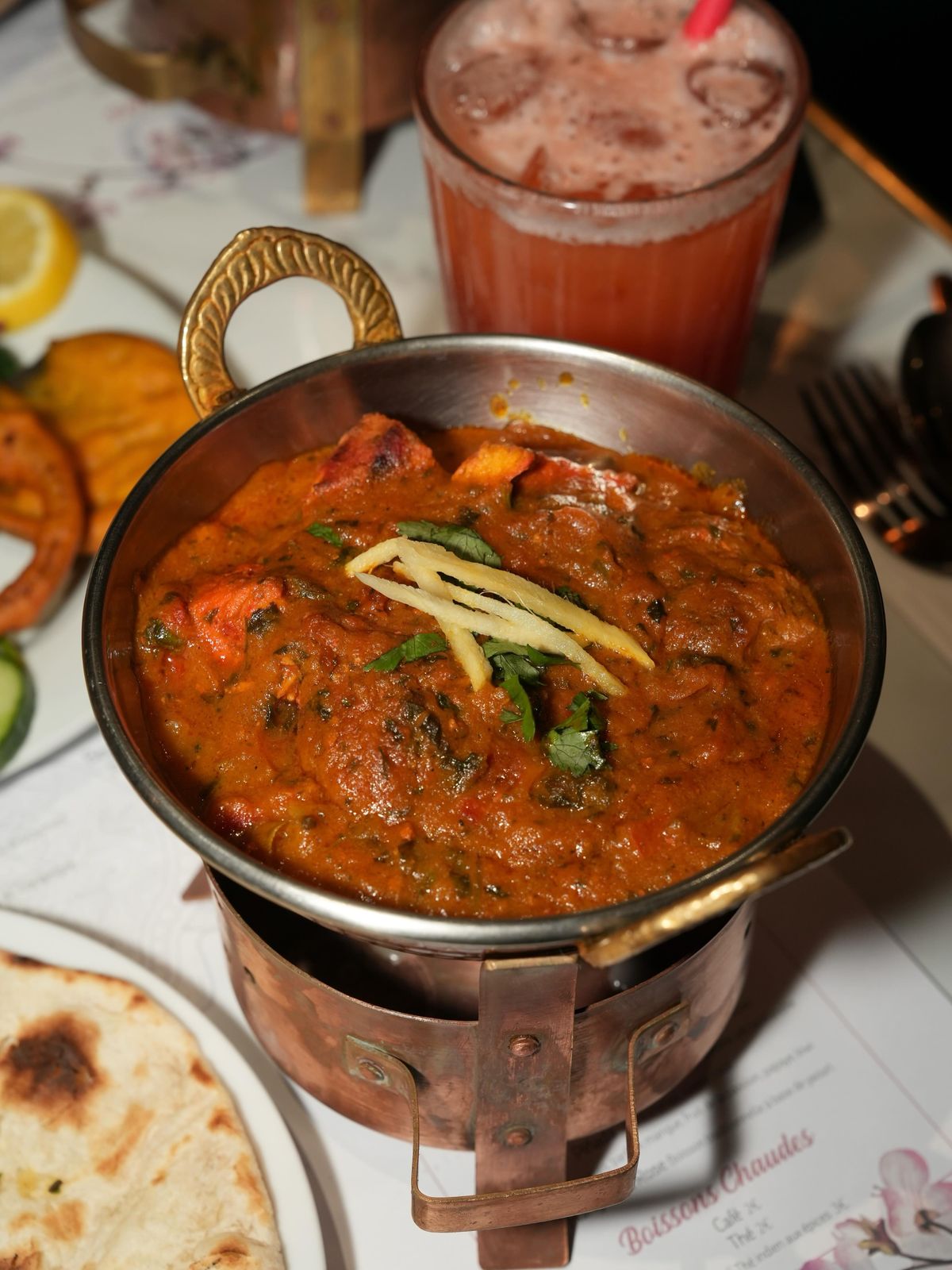 Curry mijoté servi dans sa marmite en cuivre, gingembre et coriandre fraîche, naan à côté